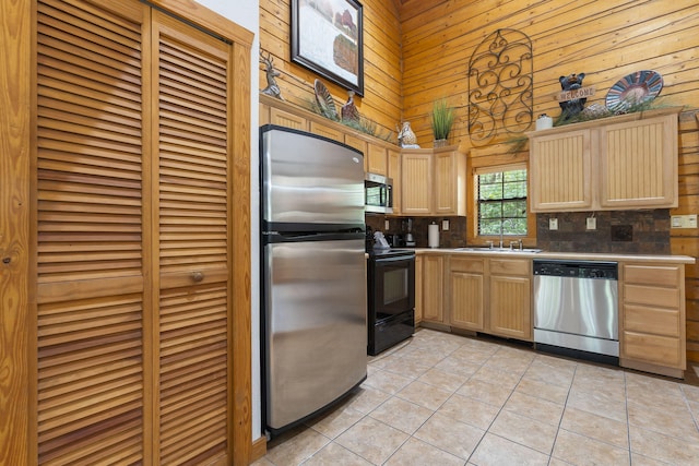 kitchen featuring light tile patterned flooring, wood walls, sink, appliances with stainless steel finishes, and light brown cabinetry