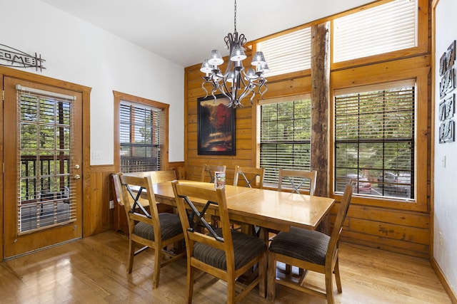 dining area with light hardwood / wood-style flooring, a chandelier, and wooden walls