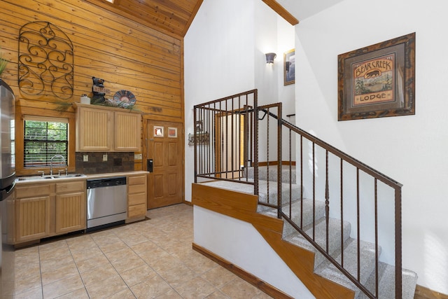 kitchen featuring high vaulted ceiling, wooden walls, sink, and dishwasher