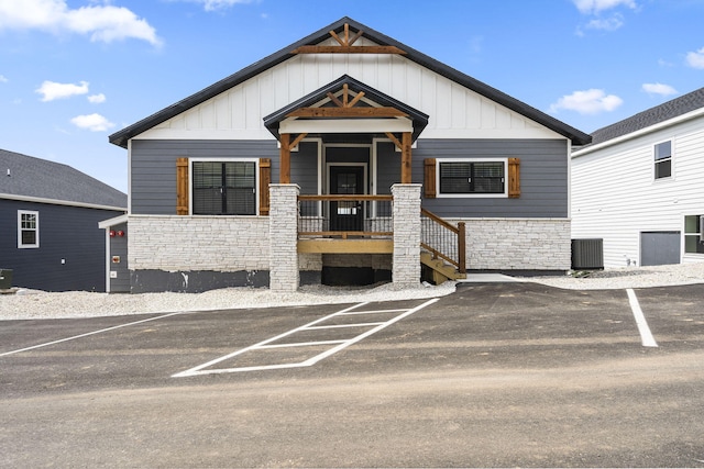 view of front facade featuring board and batten siding, central air condition unit, stone siding, and uncovered parking