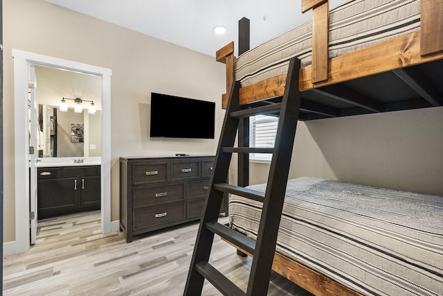 bedroom with light wood-type flooring, baseboards, ensuite bathroom, and a sink