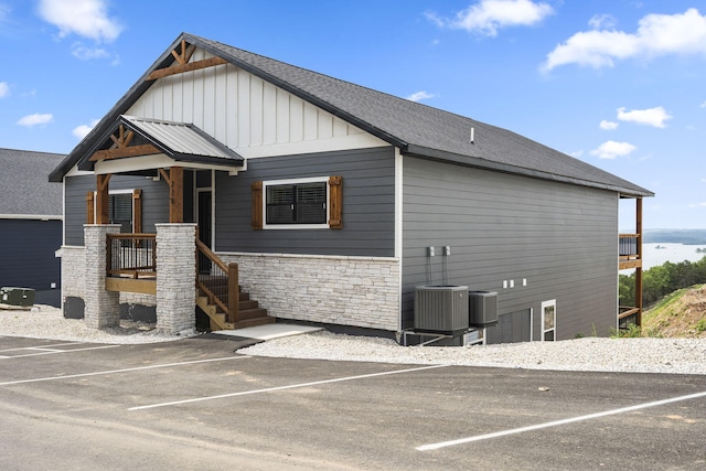 view of front of property featuring stone siding, uncovered parking, board and batten siding, and central AC
