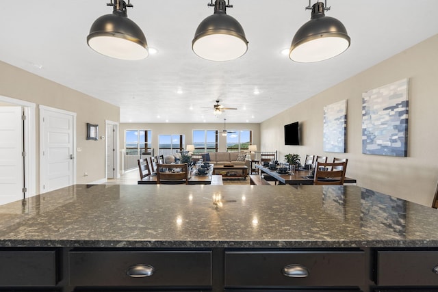 kitchen with a kitchen island, dark stone countertops, ceiling fan, and hanging light fixtures