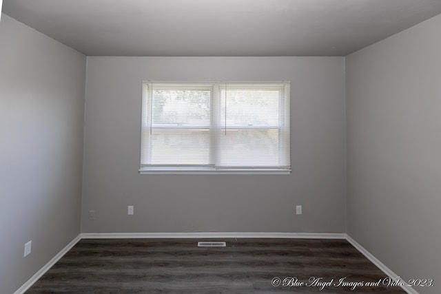 spare room with wood finished floors, visible vents, and baseboards
