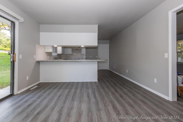 kitchen featuring a peninsula, baseboards, tasteful backsplash, and dark wood-style flooring