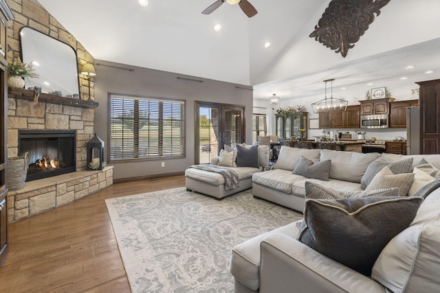 living room featuring a fireplace, high vaulted ceiling, ceiling fan, and light wood-type flooring