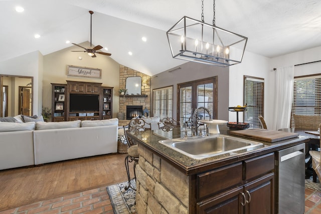 kitchen featuring a fireplace, sink, a kitchen island with sink, stainless steel dishwasher, and dark brown cabinets