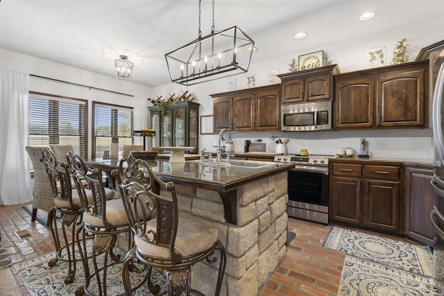 kitchen with dark brown cabinetry, a breakfast bar, sink, appliances with stainless steel finishes, and a kitchen island with sink