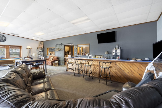 carpeted living room featuring a barn door, crown molding, and bar area