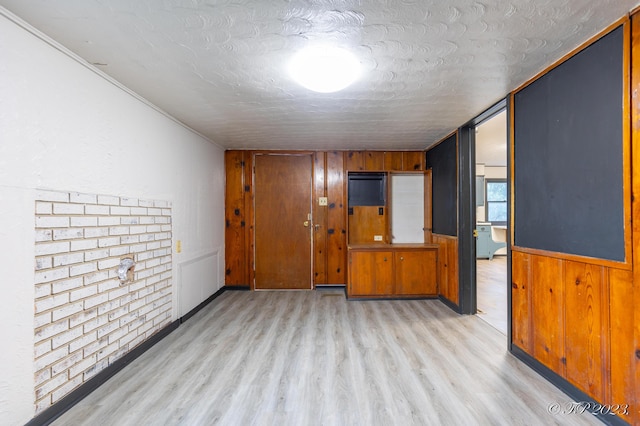 unfurnished room featuring a textured ceiling, wooden walls, and light wood-type flooring