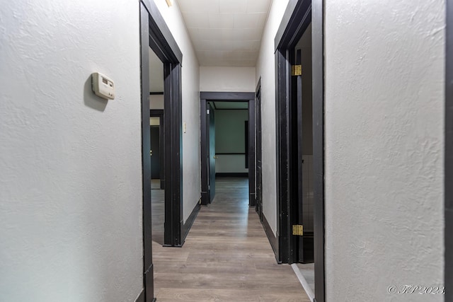 hall featuring a textured wall, baseboards, and wood finished floors