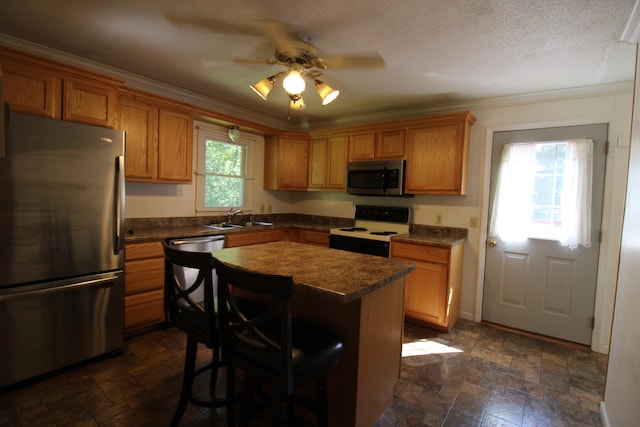 kitchen with ceiling fan, a kitchen island, sink, stainless steel appliances, and a textured ceiling