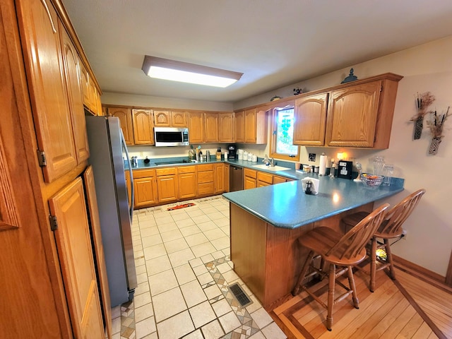 kitchen with light tile patterned flooring, sink, kitchen peninsula, appliances with stainless steel finishes, and a kitchen breakfast bar