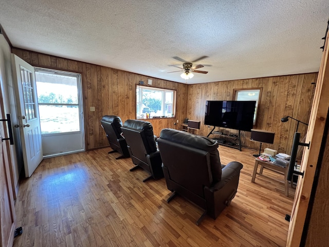 living room with wooden walls, a textured ceiling, light wood-style floors, and ceiling fan