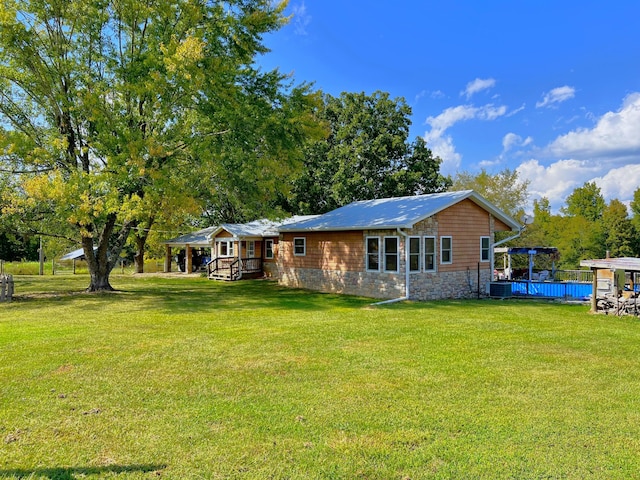 rear view of property with a yard, central AC, stone siding, and an outdoor pool