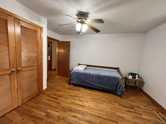 bedroom featuring baseboards, visible vents, a ceiling fan, wood finished floors, and a closet