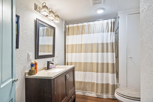 full bathroom with hardwood / wood-style flooring, vanity, shower / bath combination with curtain, a textured ceiling, and toilet