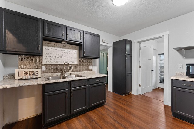 kitchen with dark hardwood / wood-style floors, sink, backsplash, light stone counters, and a textured ceiling