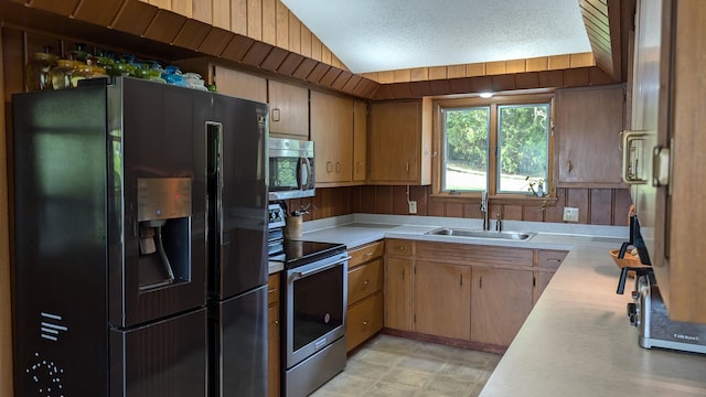 kitchen with lofted ceiling, wood walls, sink, a textured ceiling, and stainless steel appliances