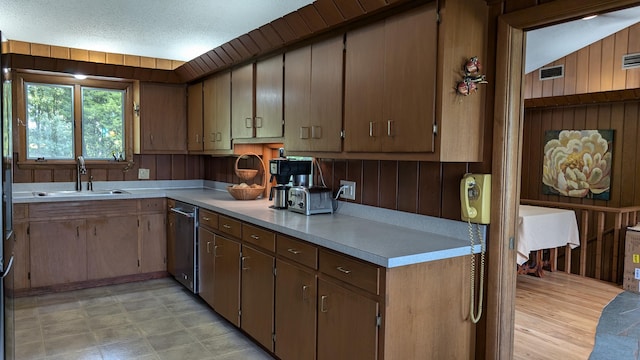 kitchen featuring wood walls, sink, lofted ceiling, stainless steel dishwasher, and a textured ceiling