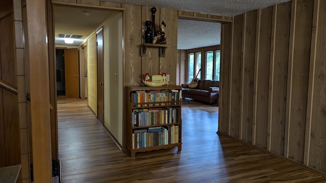 corridor featuring a textured ceiling, wooden walls, and dark hardwood / wood-style flooring