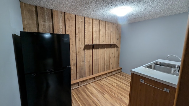 kitchen with wood walls, sink, a textured ceiling, light wood-type flooring, and black refrigerator