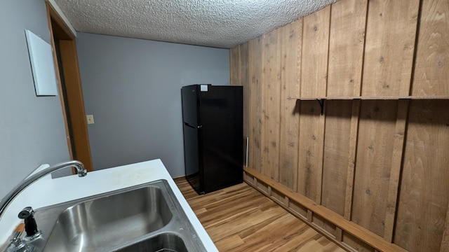 kitchen with sink, light wood-type flooring, black refrigerator, and a textured ceiling