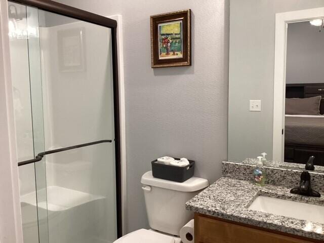 bathroom featuring a shower with door, vanity, and toilet