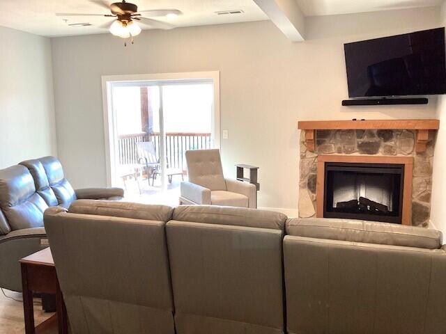 living room with ceiling fan, beamed ceiling, and a fireplace