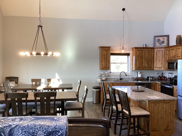 kitchen with hanging light fixtures, sink, dark hardwood / wood-style floors, a center island, and light stone countertops