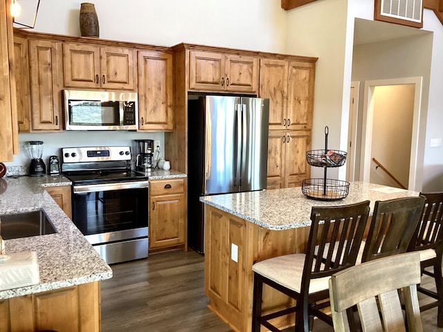 kitchen featuring appliances with stainless steel finishes, light stone counters, dark hardwood / wood-style floors, and a breakfast bar