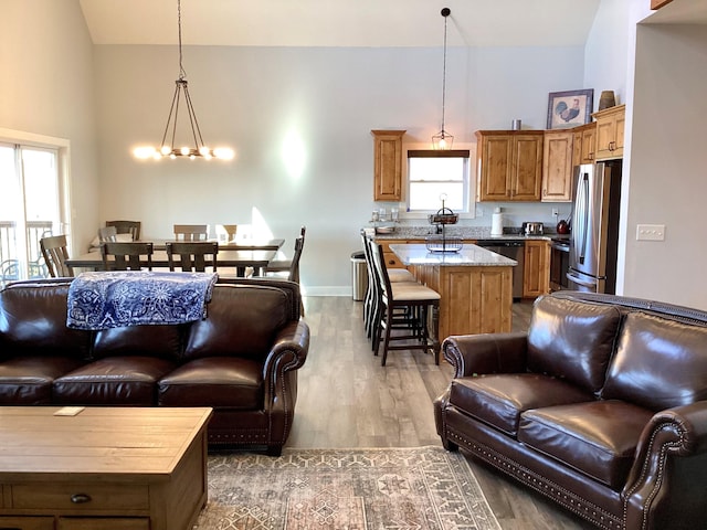 living room with plenty of natural light, light hardwood / wood-style floors, high vaulted ceiling, and an inviting chandelier