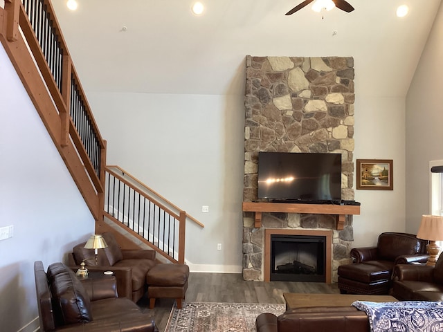 living room with wood-type flooring, a stone fireplace, lofted ceiling, and ceiling fan