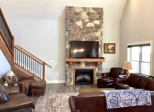 living room featuring wood-type flooring, a stone fireplace, and vaulted ceiling