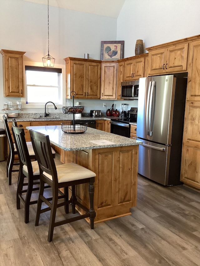 kitchen with light stone counters, stainless steel appliances, hardwood / wood-style floors, and a center island