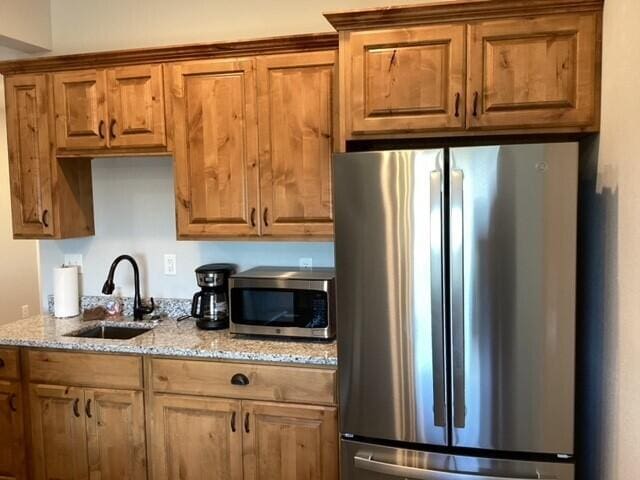 kitchen featuring light stone countertops, appliances with stainless steel finishes, and sink