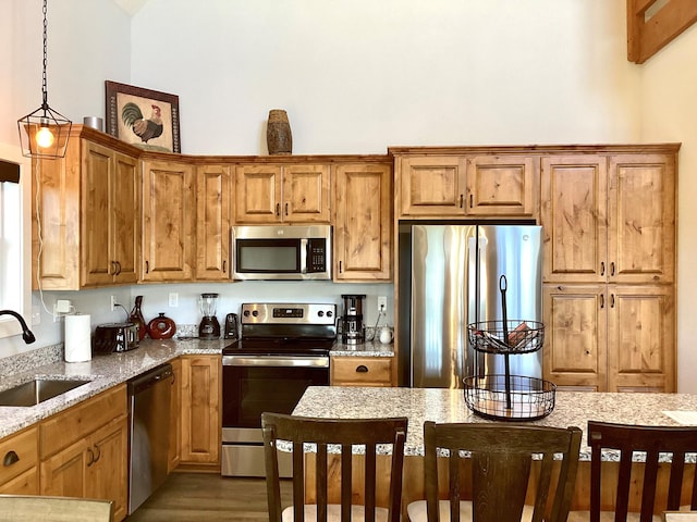 kitchen featuring light stone countertops, hardwood / wood-style floors, sink, appliances with stainless steel finishes, and decorative light fixtures