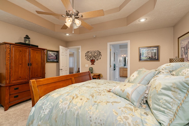 bedroom featuring light colored carpet, a raised ceiling, a textured ceiling, and ensuite bathroom