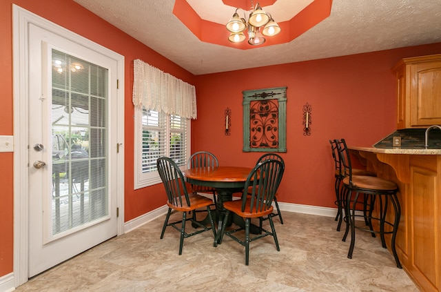 dining area featuring a raised ceiling, a textured ceiling, and a notable chandelier