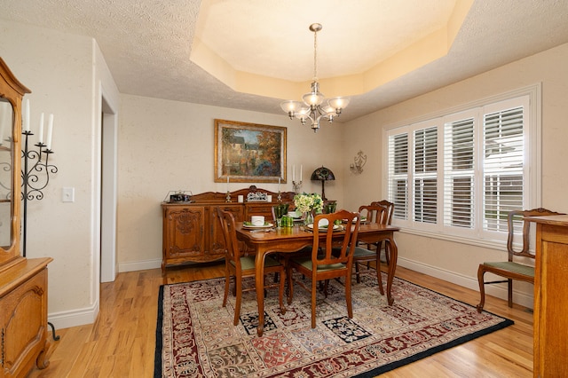 dining room featuring a raised ceiling, a textured ceiling, light hardwood / wood-style flooring, and a notable chandelier