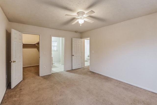 unfurnished bedroom featuring a spacious closet, ceiling fan, a closet, light colored carpet, and a textured ceiling