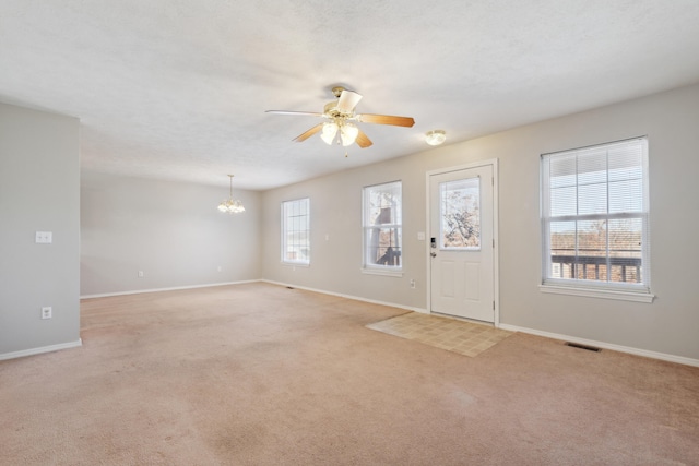 carpeted entrance foyer with ceiling fan with notable chandelier, a textured ceiling, and a healthy amount of sunlight