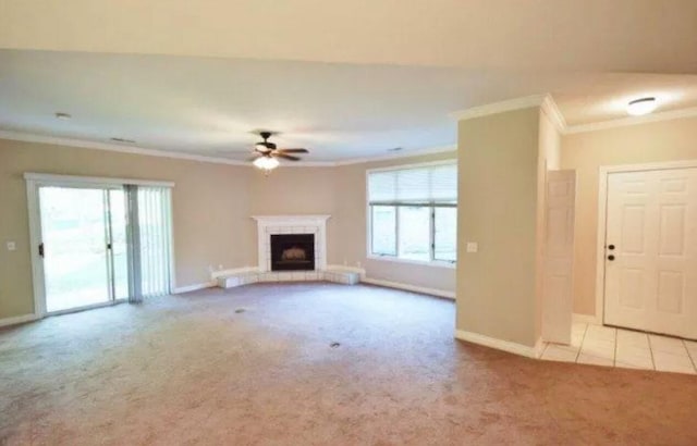 unfurnished living room with a fireplace with raised hearth, a ceiling fan, carpet floors, crown molding, and baseboards