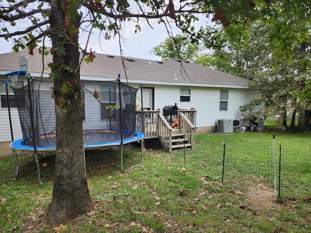 rear view of property featuring a trampoline, central air condition unit, a wooden deck, and a lawn