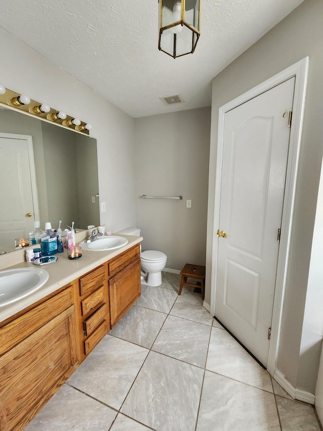 bathroom featuring vanity, toilet, a textured ceiling, and tile patterned floors