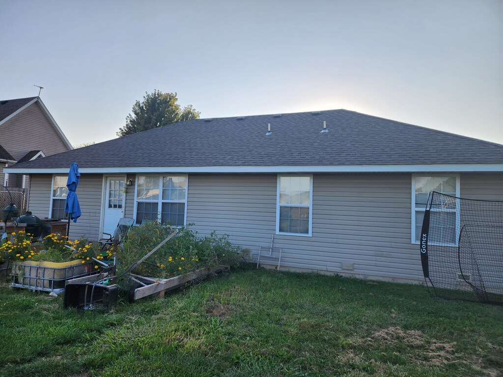 1211 Woodland, Monett, MO 65708 - back of house with a lawn, a shingled roof, and a vegetable garden