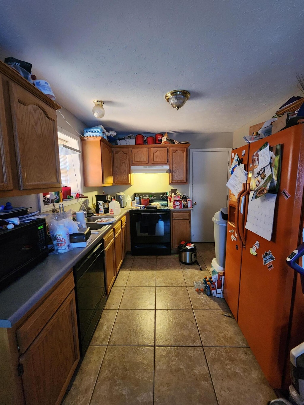 1211 Woodland, Monett, MO 65708 - kitchen featuring brown cabinetry, black appliances, under cabinet range hood, and light tile patterned floors
