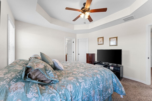 carpeted bedroom featuring a raised ceiling and ceiling fan