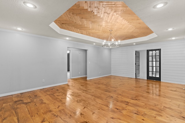 spare room featuring wooden walls, a raised ceiling, and light hardwood / wood-style flooring