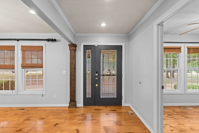 entrance foyer featuring ornate columns, crown molding, plenty of natural light, and light hardwood / wood-style floors